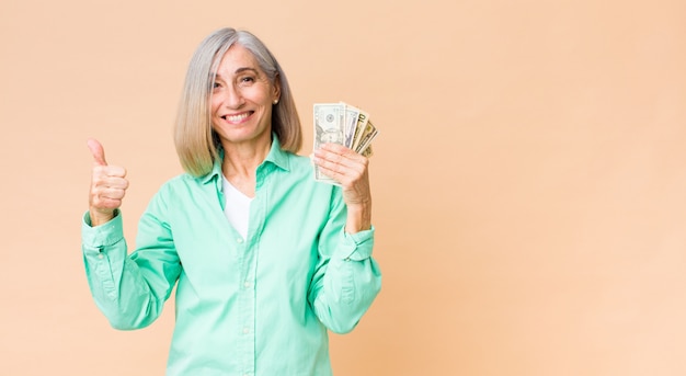 Donna di mezza età con le banconote del dollaro sulla parete dello spazio della copia