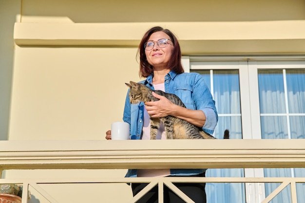 Donna di mezza età con un gatto sotto il portico della casa