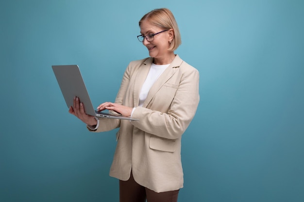 Donna di mezza età d'affari in una giacca con un computer portatile per lavorare su uno sfondo di studio con spazio di copia