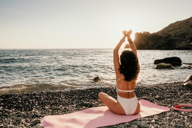 Donna di mezza età di bell'aspetto in costume da bagno bianco e bracciali in stile boho che praticano all'aperto lo yoga