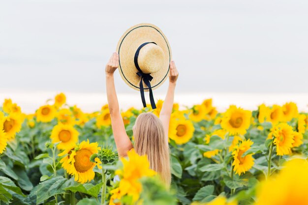 Donna di mezza età felice che cammina nel cappello della tenuta del campo di girasole in fiore