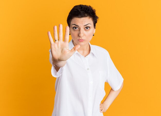 Donna di mezza età impressionata che tiene la mano sulla vita guardando la telecamera facendo il gesto di arresto