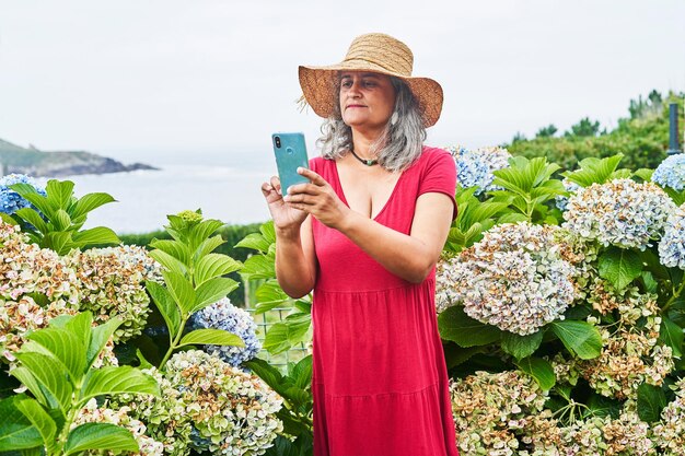 Donna di mezza età in abito rosso per scattare foto con il telefono cellulare vicino al mare