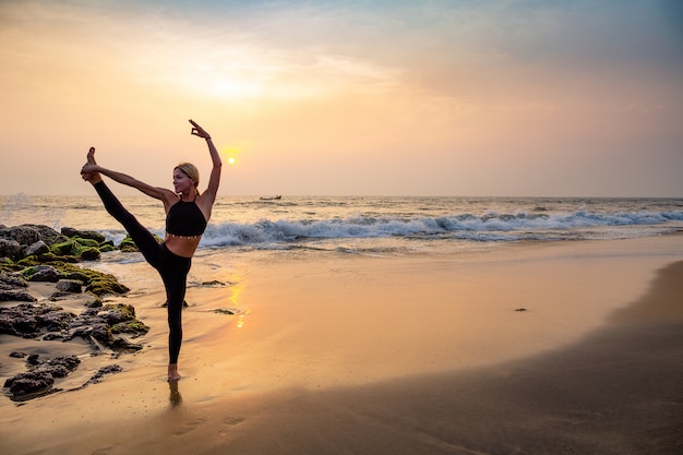 Donna di mezza età in nero facendo yoga su una spiaggia di sabbia