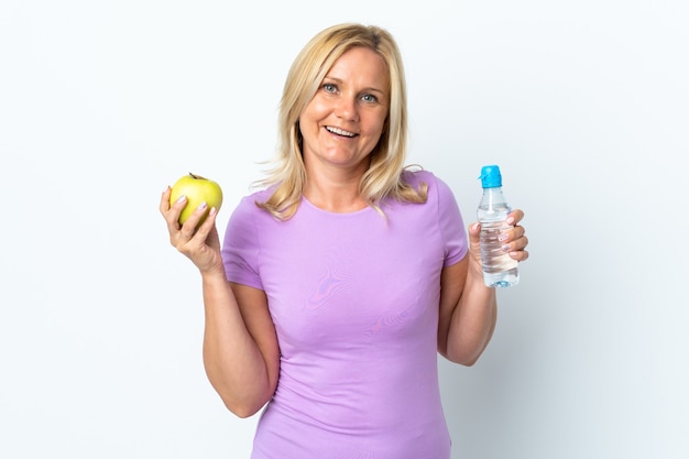Donna di mezza età isolata sul muro bianco con una mela e con una bottiglia d'acqua