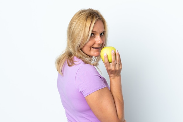 Donna di mezza età isolata sulla parete bianca che mangia una mela
