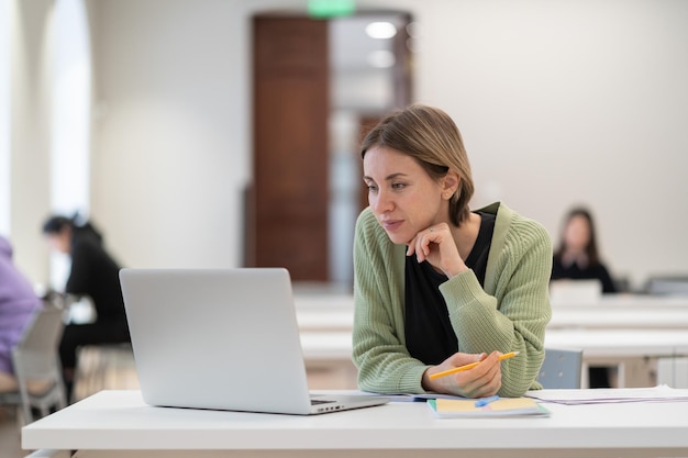 Donna di mezza età pensierosa che studia in biblioteca sul computer portatile studentessa matura che guarda webinar