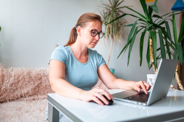 Donna di mezza età seduta al tavolo a casa che lavora utilizzando il computer portatile. Lavora da casa e resta a casa durante il concetto di pandemia di coronovirus