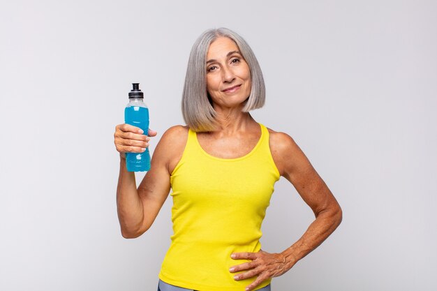 Donna di mezza età sorridente felicemente con una mano sul fianco e atteggiamento fiducioso, positivo, orgoglioso e amichevole. concetto di fitness