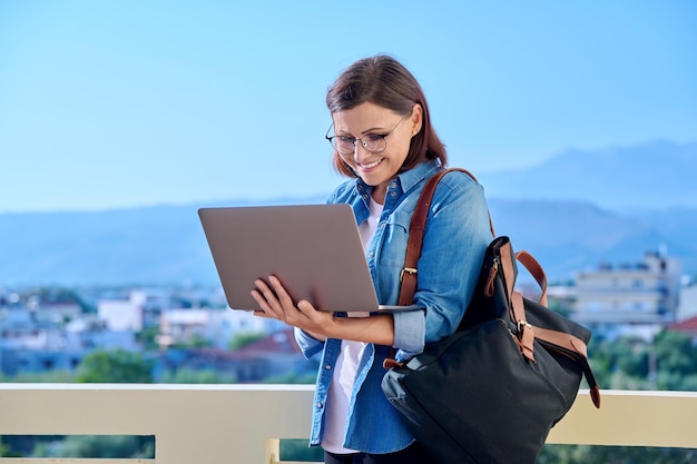 Donna di mezza età sorridente positiva di affari con il computer portatile all'aperto