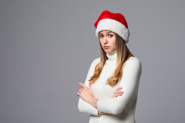 Donna di Natale offesa con un cappello da Babbo Natale isolato su un muro grigio