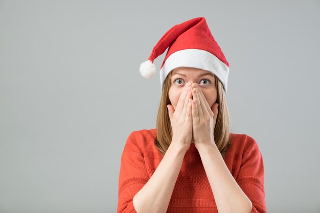 Donna di natale scioccata che indossa un cappello da Babbo Natale isolato su uno sfondo grigio