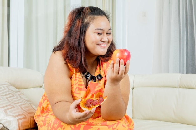 Donna di obesità che sceglie la mela mentre tiene la pizza