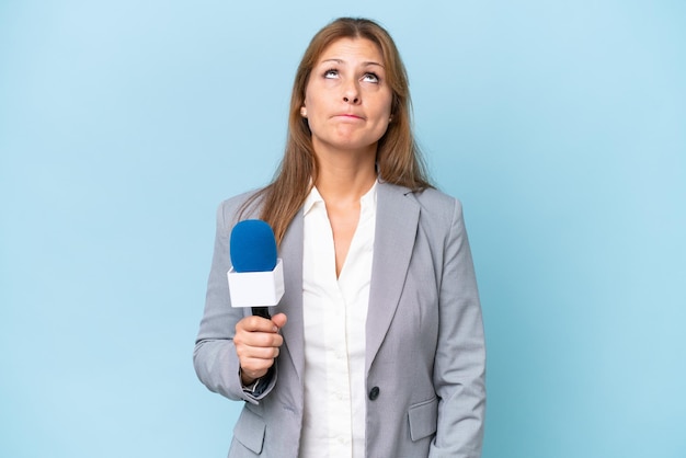 Donna di presentatrice televisiva di mezza età su sfondo blu isolato e alzando lo sguardo