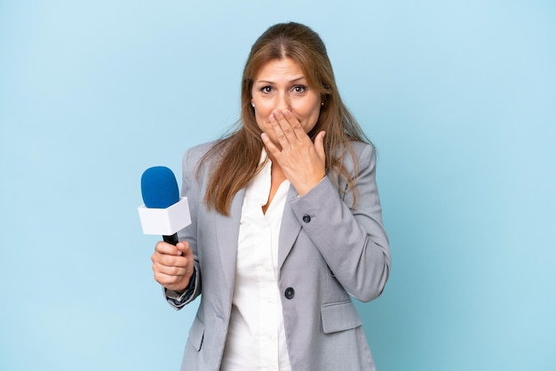 Donna di presentatrice televisiva di mezza età su sfondo blu isolato felice e sorridente che copre la bocca con la mano