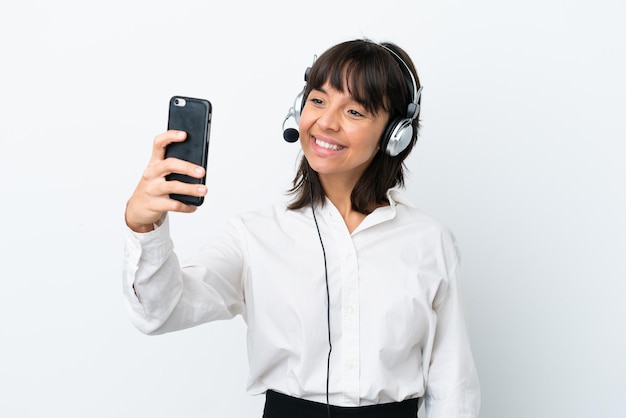 Donna di razza mista di telemarketing che lavora con un auricolare isolato su sfondo bianco che fa un selfie