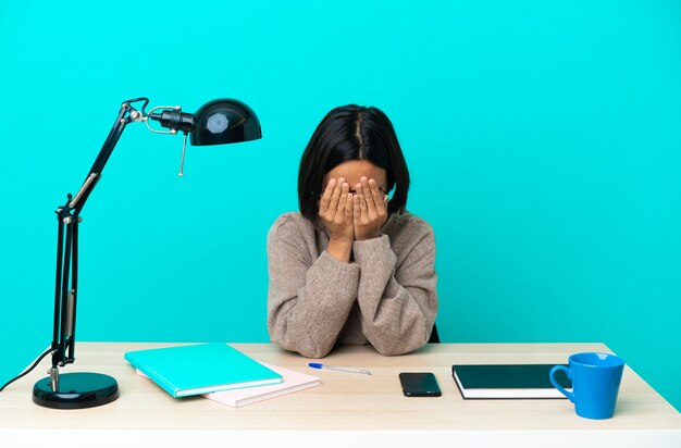 Donna di razza mista giovane studente studiando su un tavolo che copre gli occhi con le mani