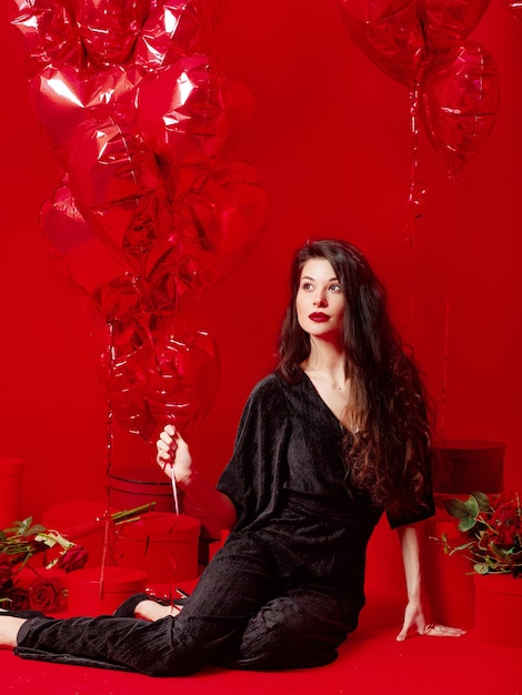 Donna di San Valentino in nero con palloncini rossi a forma di cuore divertendosi