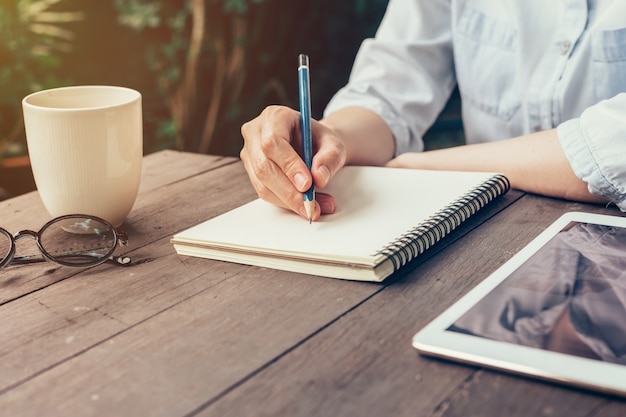 Donna di scrittura di scrittura a mano sulla tavola di legno in caffè.