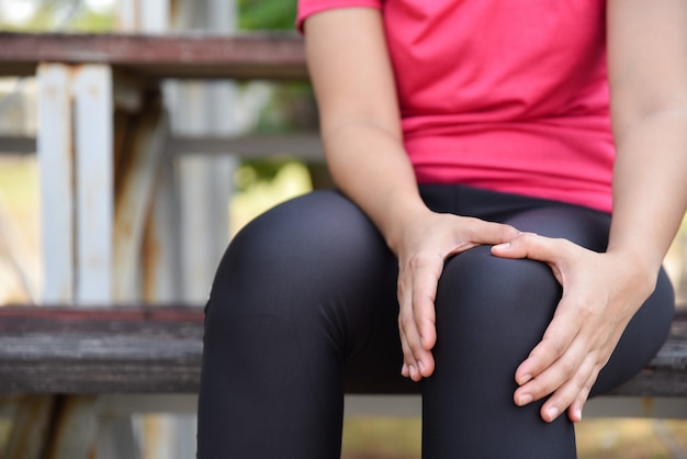 Donna di sport che soffre dal ginocchio corrente durante l&#39;allenamento all&#39;aperto e seduto alle gradinate.