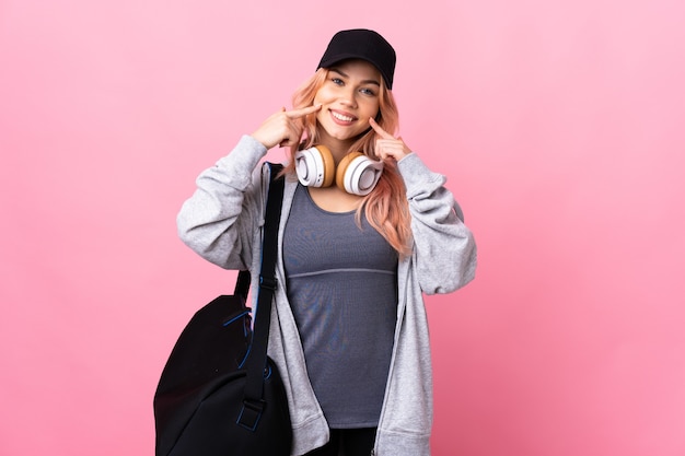 Donna di sport dell'adolescente con borsa sportiva sopra la parete isolata che sorride con un'espressione felice e piacevole