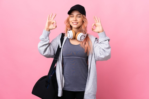 Donna di sport dell'adolescente con la borsa di sport sopra la parete isolata nella posa di zen