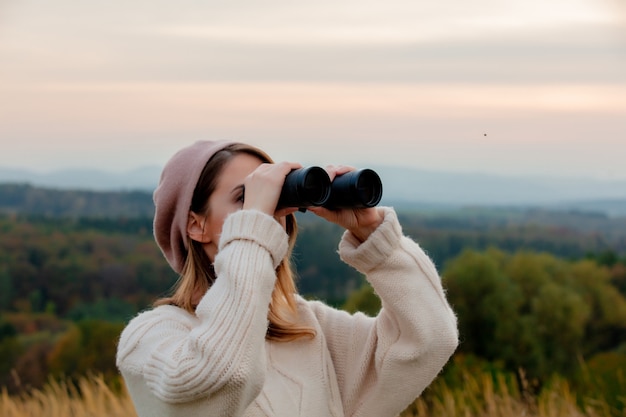 Donna di stile con il binocolo in campagna con le montagne