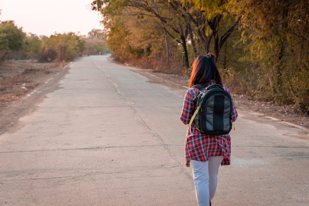 Donna di viaggio con lo zaino che cammina sulla campagna della strada asfaltata