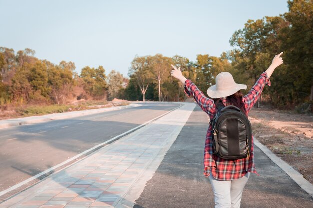 Donna di viaggio con lo zaino che cammina sulla campagna della strada asfaltata