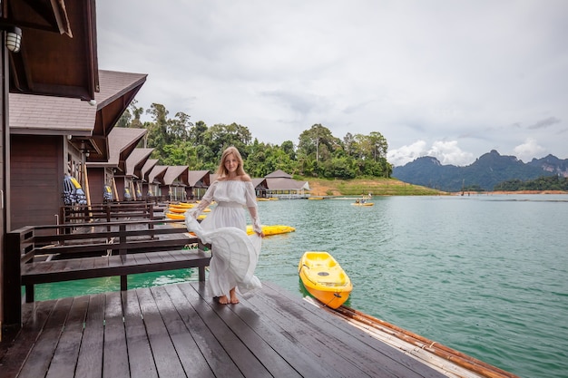 Donna di viaggio in piedi sul molo della casa in legno sul lago con montagne tropicali