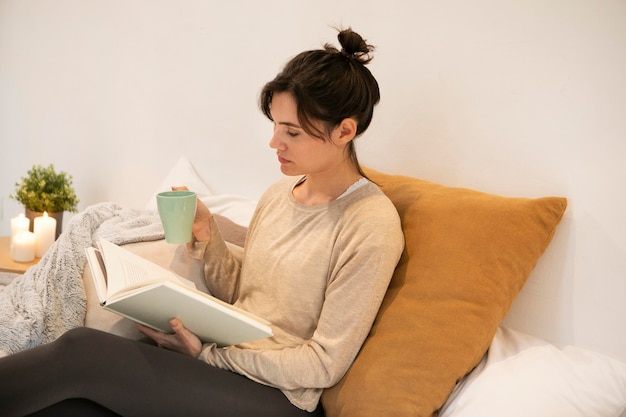 Donna di vista laterale che tiene una tazza di caffè e che legge un libro