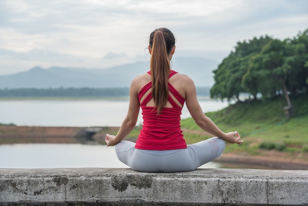 Donna di yoga che fa meditazione nel lago, vista posteriore.