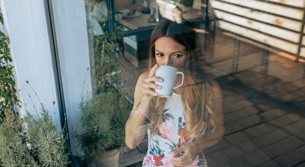 Donna dietro la finestra che beve caffè