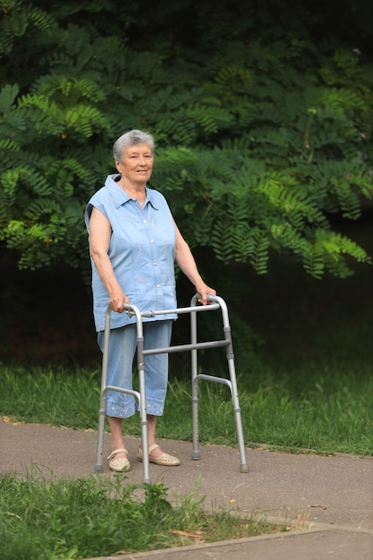 Donna disabile anziana felice che cammina con il camminatore all'aperto in estate