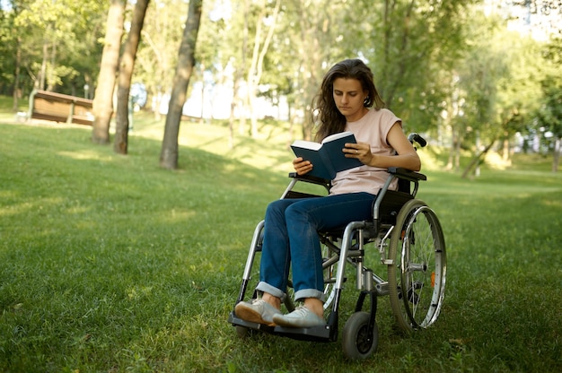 Donna disabile in sedia a rotelle che legge un libro in parco. Paralitici e disabilità, superamento dell'handicap. La persona di sesso femminile handicappata si diverte all'aperto