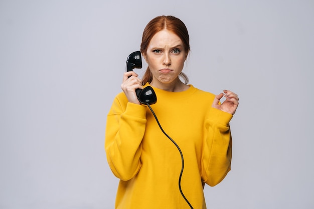 Donna dispiaciuta in maglione giallo che tiene il ricevitore del telefono retrò e guarda la telecamera