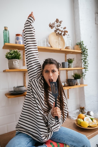 Donna divertente che canta nella spatola che tiene la spatola come microfono