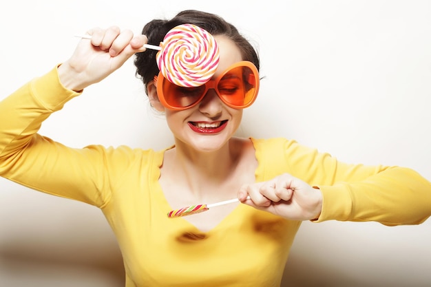 Donna divertente che indossa grandi occhiali arancioni con in mano un grande lecca-lecca Bir