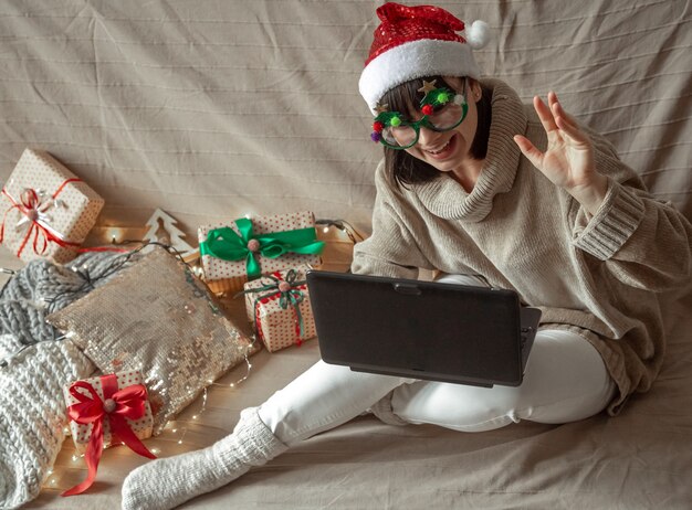 Donna divertente in bicchieri di Natale e cappello di Babbo Natale si siede a un computer portatile