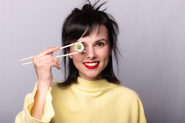 Donna divertente in un maglione giallo che mangia sushi Sushi su bastoncini