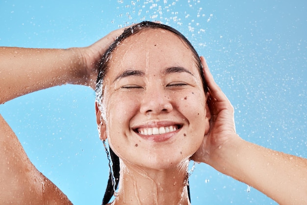 Donna doccia e sorriso per l'igiene della cura della pelle lavare o pulire su uno sfondo blu studio Felice volto femminile sorridente di soddisfazione per cosmetici benessere puliti o trattamenti per la cura dei capelli sani
