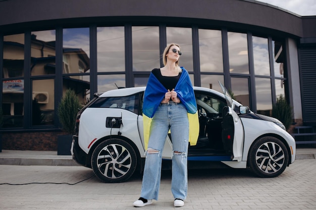 Donna donna con la bandiera dell'Ucraina che carica un'auto elettrica presso la stazione di servizio elettrica