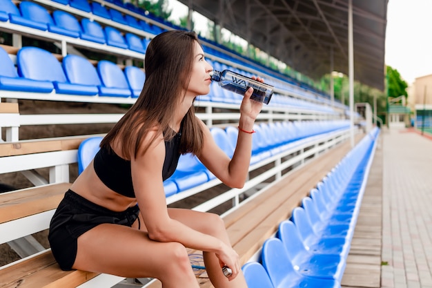 Donna durante la pausa tra allenamento sportivo sullo stadio seduto su una panchina