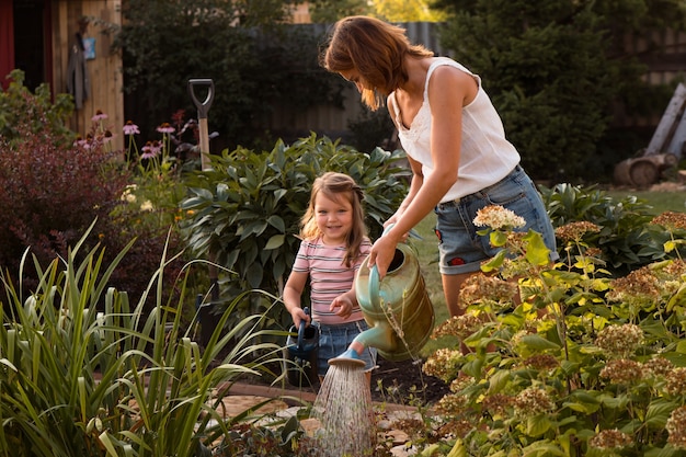 Donna e bambina che lavorano insieme in giardino innaffiando fiori in estate day