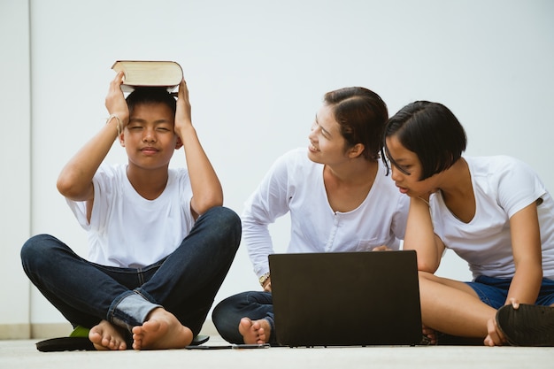 Donna e bambini dell&#39;Asia che utilizzano insieme computer e libro di lettura