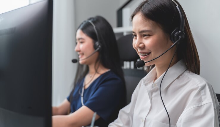 Donna e gruppo di affari asiatici sorridenti che lavorano nella call center alla scrivania con la cuffia avricolare e il computer.