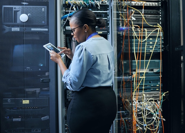 Donna e ingegnere della sala server con tablet per la programmazione della sicurezza informatica o la manutenzione dei cavi Tecnico donna nera nel datacenter per software di rete o aggiornamento del sistema con app IT e internet