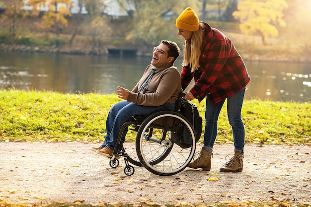Donna e la sua amica su una sedia a rotelle che passeggiano attraverso il parco in un fiume godendosi l'autunno