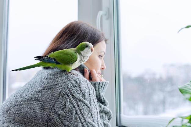 Donna e pappagallo di stile di vita domestico di inverno che guardano insieme attraverso la finestra innevata