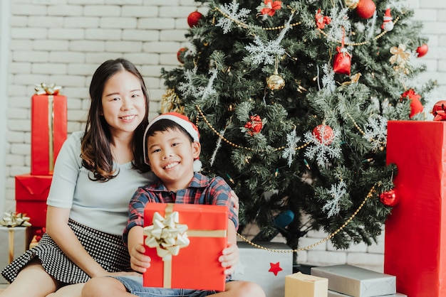 Donna e ragazzo che si siedono insieme dall'albero di Natale con i contenitori di regalo